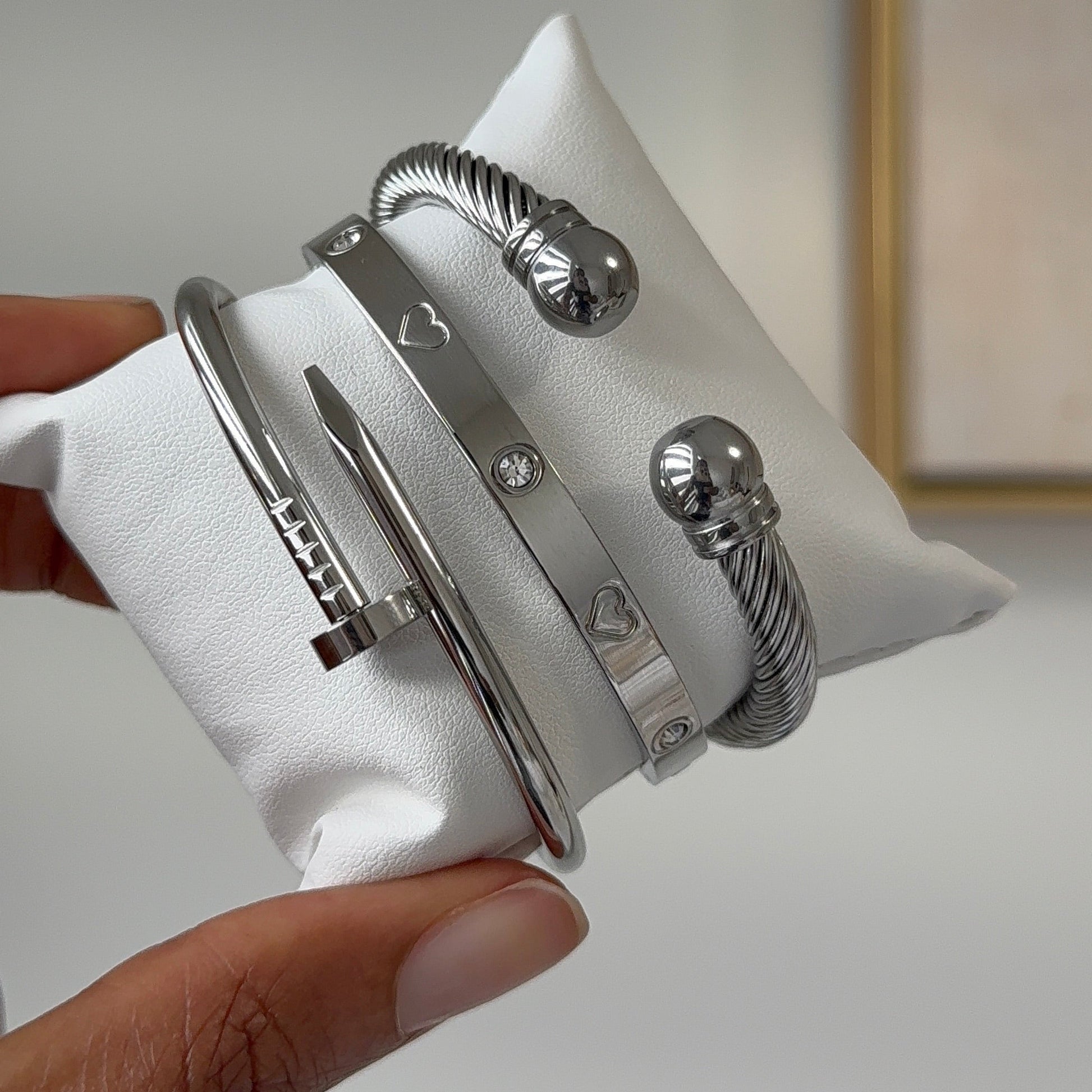 Set of silver bracelets on a white cushion held by a hand against a neutral background