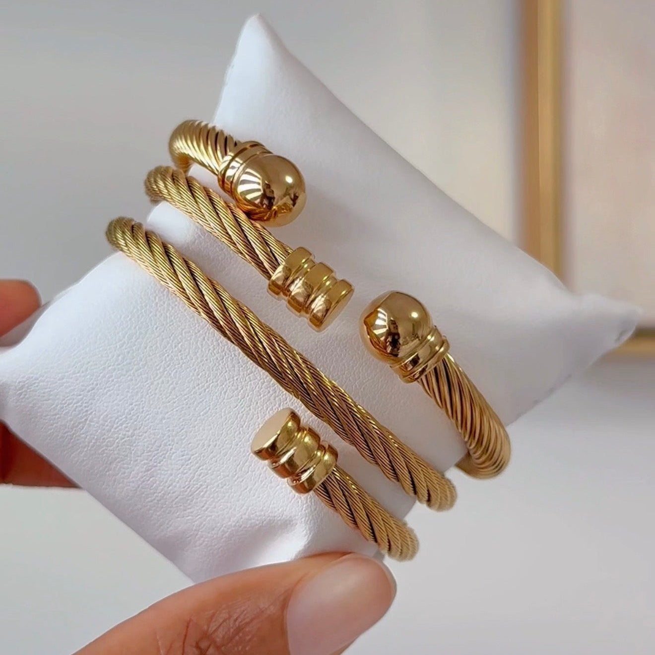 Gold bracelets on a white cushion with a blurred background