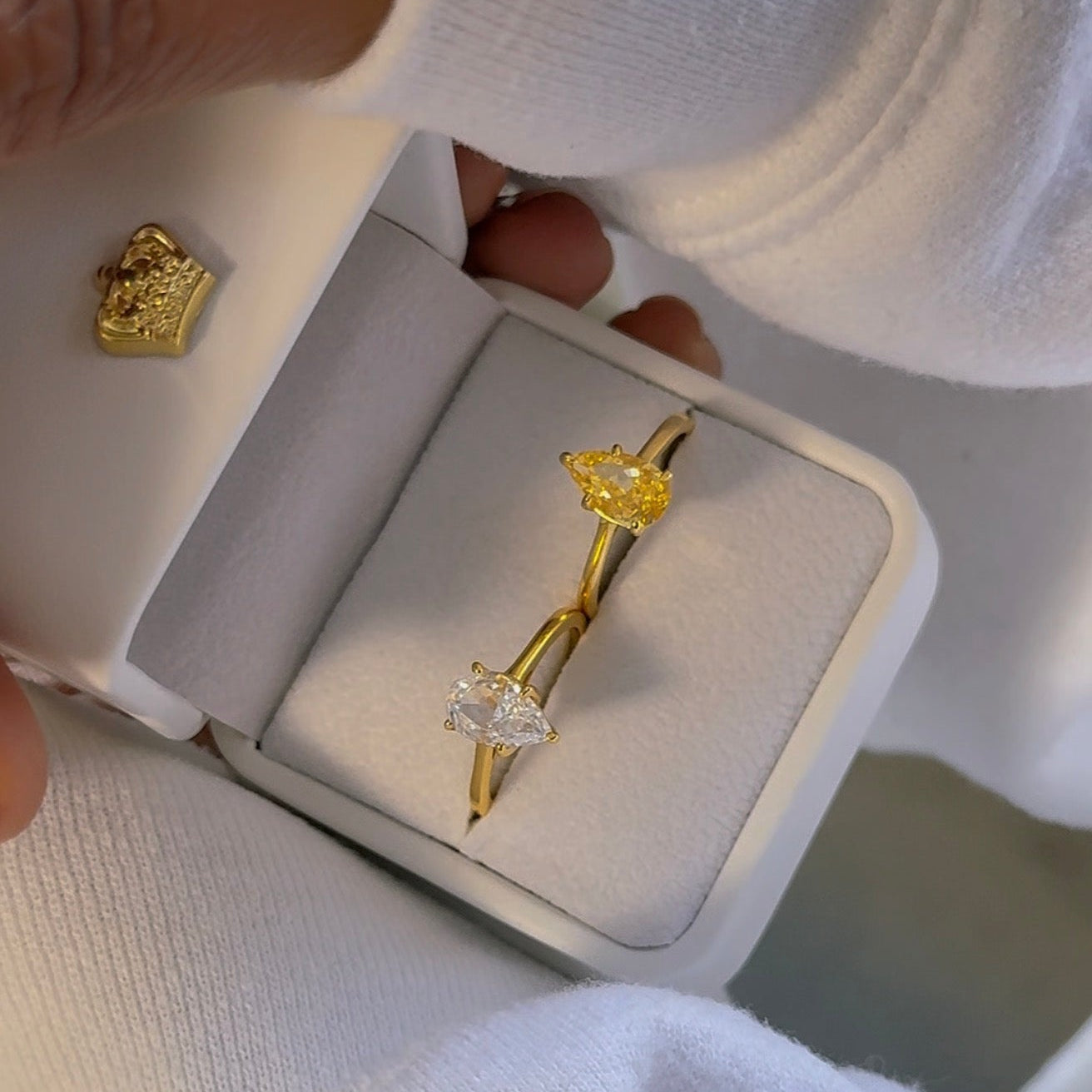 Gold bow-shaped ring with a diamond in a white box held by a person wearing a white shirt.