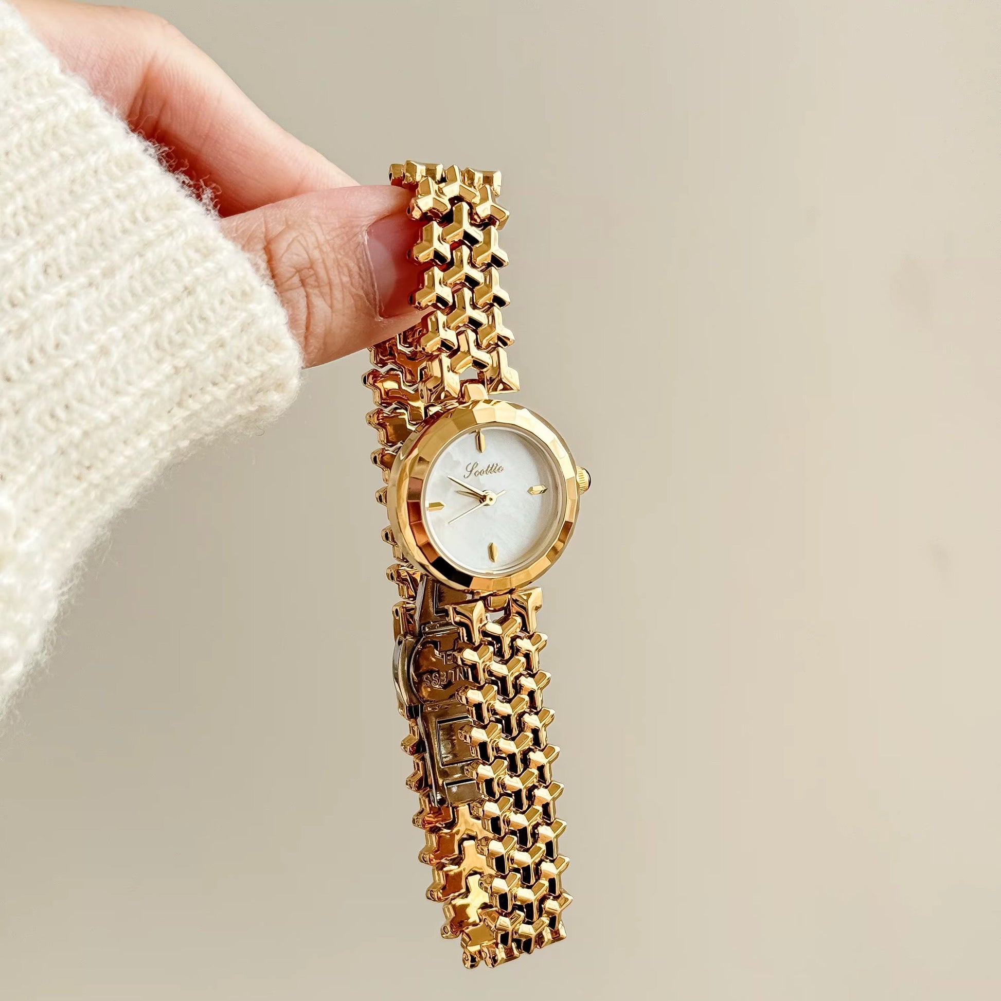 Gold chain watch held by a hand against a neutral background