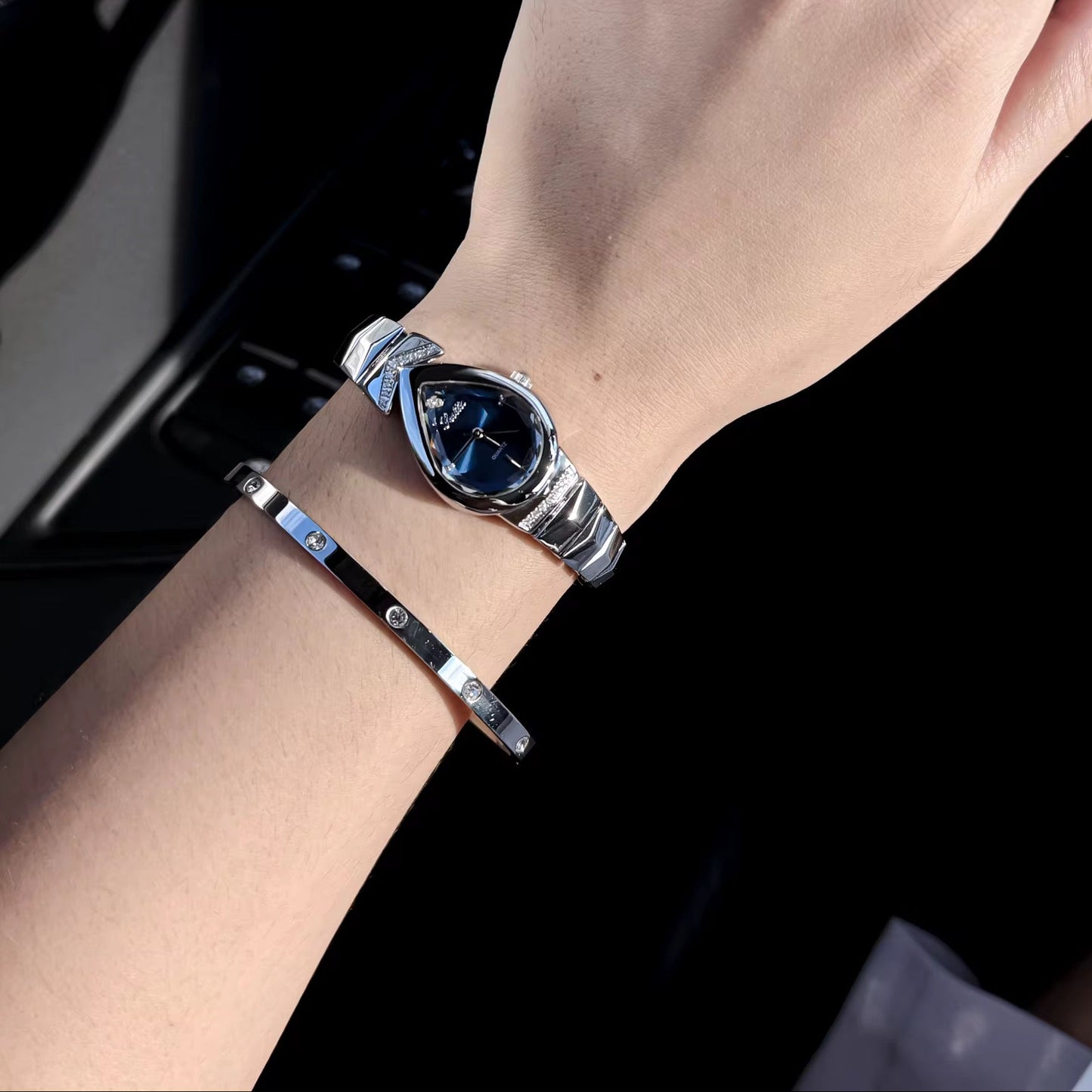 Hand wearing a silver bracelet and ring with a dark background