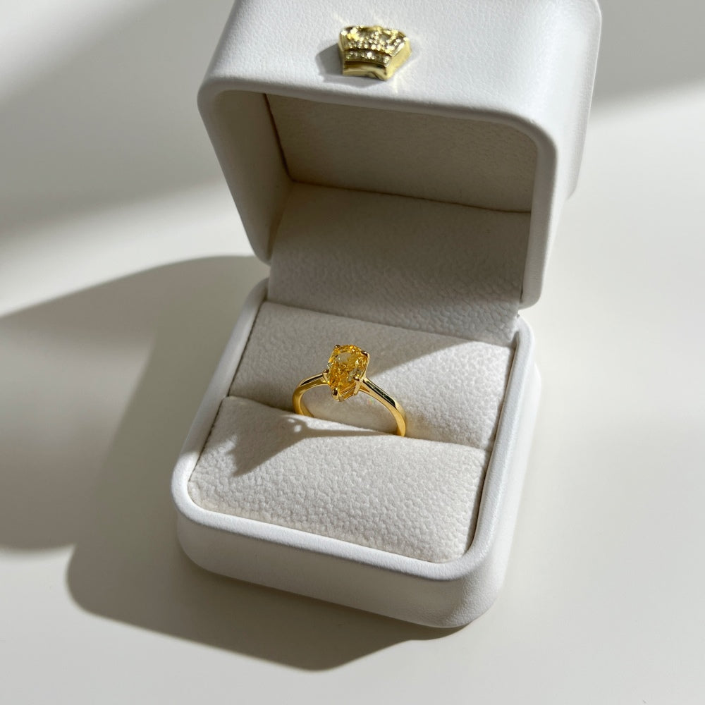 Gold ring with a yellow gemstone in an open jewelry box on a light background