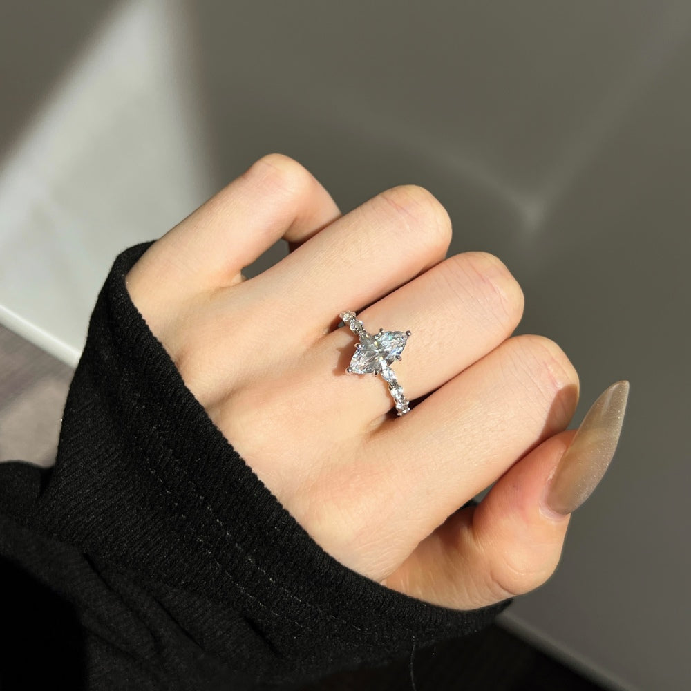 Hand wearing a silver ring with a clear gemstone against a neutral background