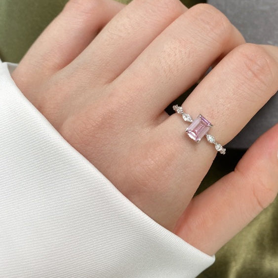 Hand wearing a pink gemstone ring with a neutral background